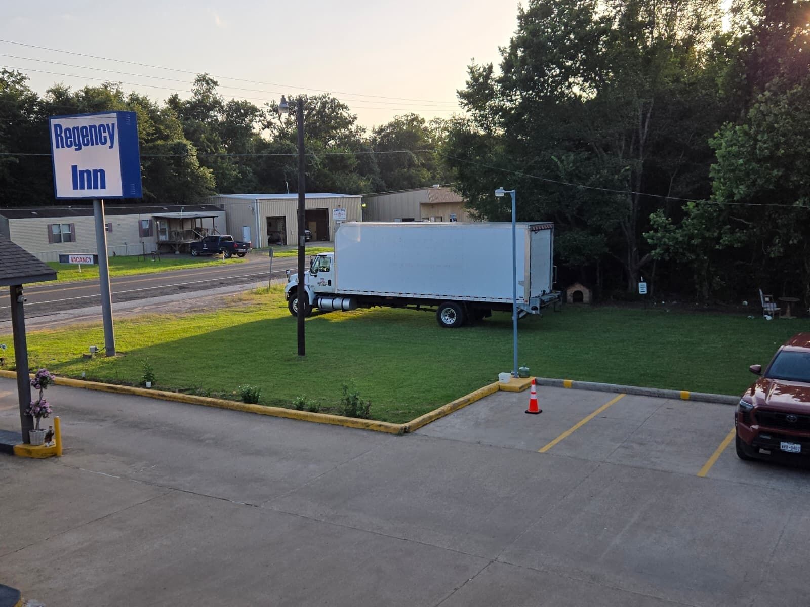 A parking lot with a sign for Regency Inn, a white truck, and a red car.