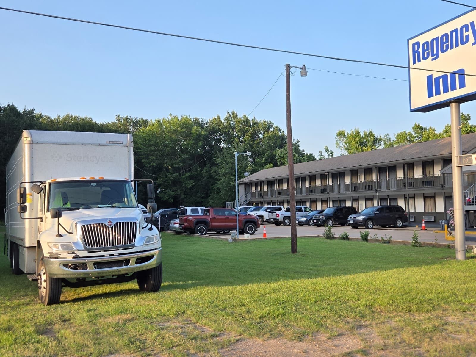 Un parking avec un grand camion, une enseigne de motel et un bâtiment doté de nombreuses fenêtres.