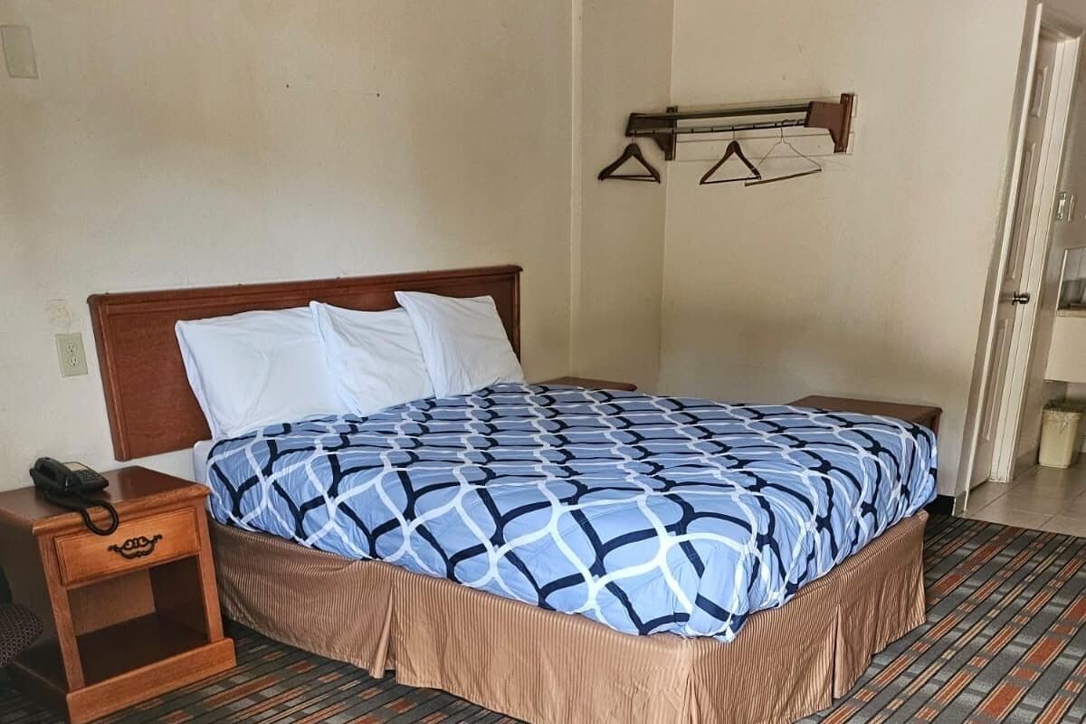 A hotel room with a bed, a nightstand, a telephone, and a wall-mounted coat rack.