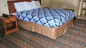 Habitación de hotel con cama, mesita de noche, teléfono y perchero en la pared.