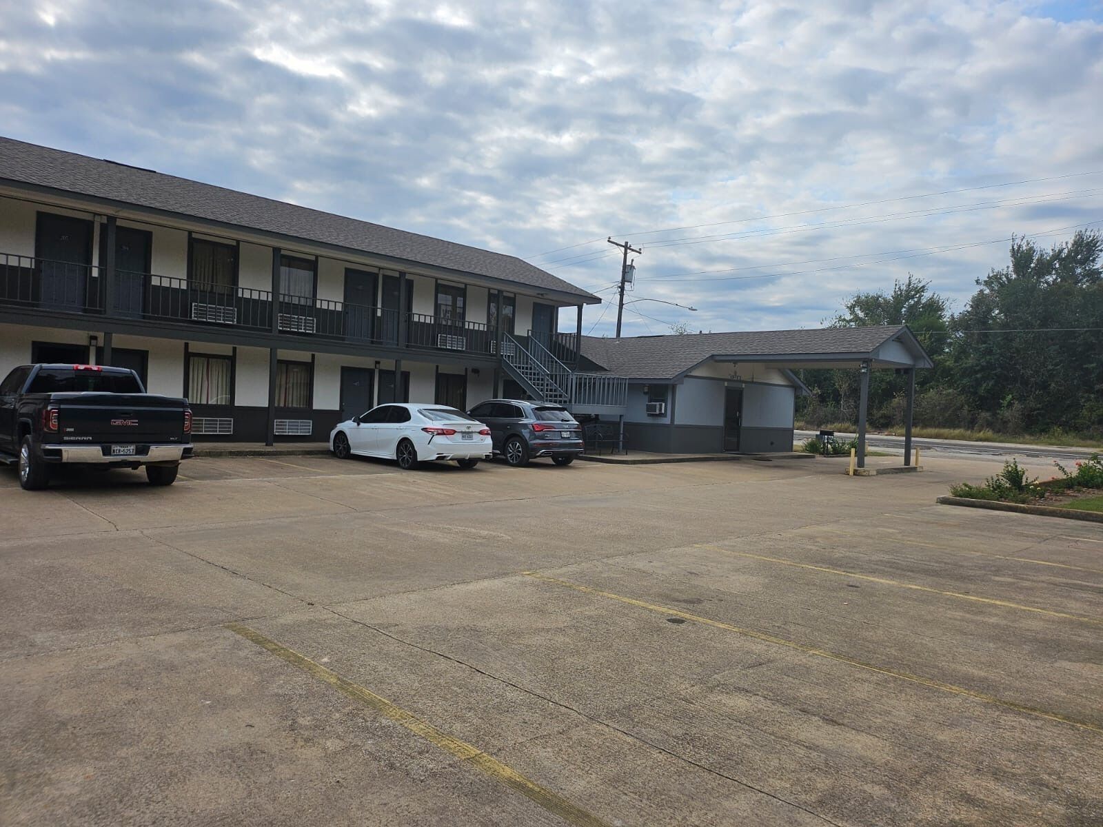 Un motel con estacionamiento, una zona techada y un edificio con balcón.