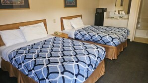 A hotel room with two beds, each with a patterned bedspread, a bedside table with a lamp, and a small desk with a microwave. - Regency Inn (Jewett)