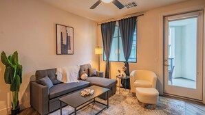 A modern living room with a sofa, armchair, coffee table, and a large window with curtains. - Scottsdale Grand (Scottsdale)