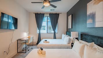 A hotel room with two beds, a desk, a TV, and a ceiling fan.