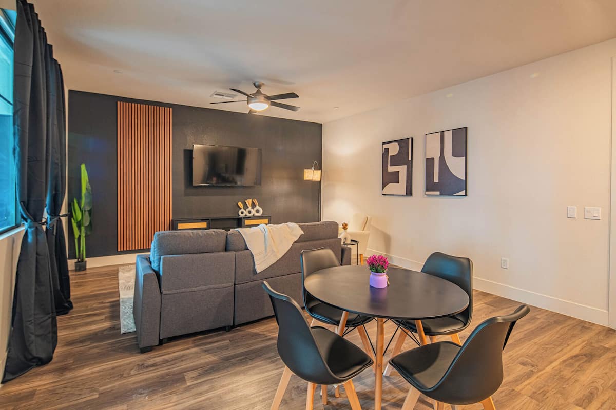 A modern living room with a gray sofa, black chairs, a round table, and a ceiling fan.