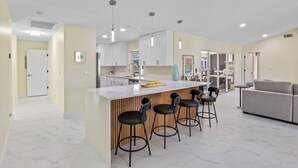 Eine moderne Küche mit weißen Schränken, einer zentralen Kochinsel mit Barhocker und einem Essbereich mit einer Couch und Stühlen.