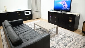 Moderni olohuone, jossa on musta nahkasohva, puinen sohvapöytä, litteänäyttöinen televisio, jääkaappi ja mikroaaltouuni.