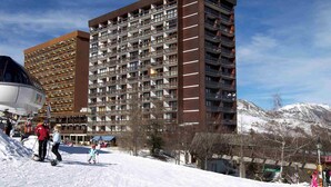 A high-rise hotel with multiple balconies and a ski resort in the background. - Baikonour by Interhome (Le Corbier)