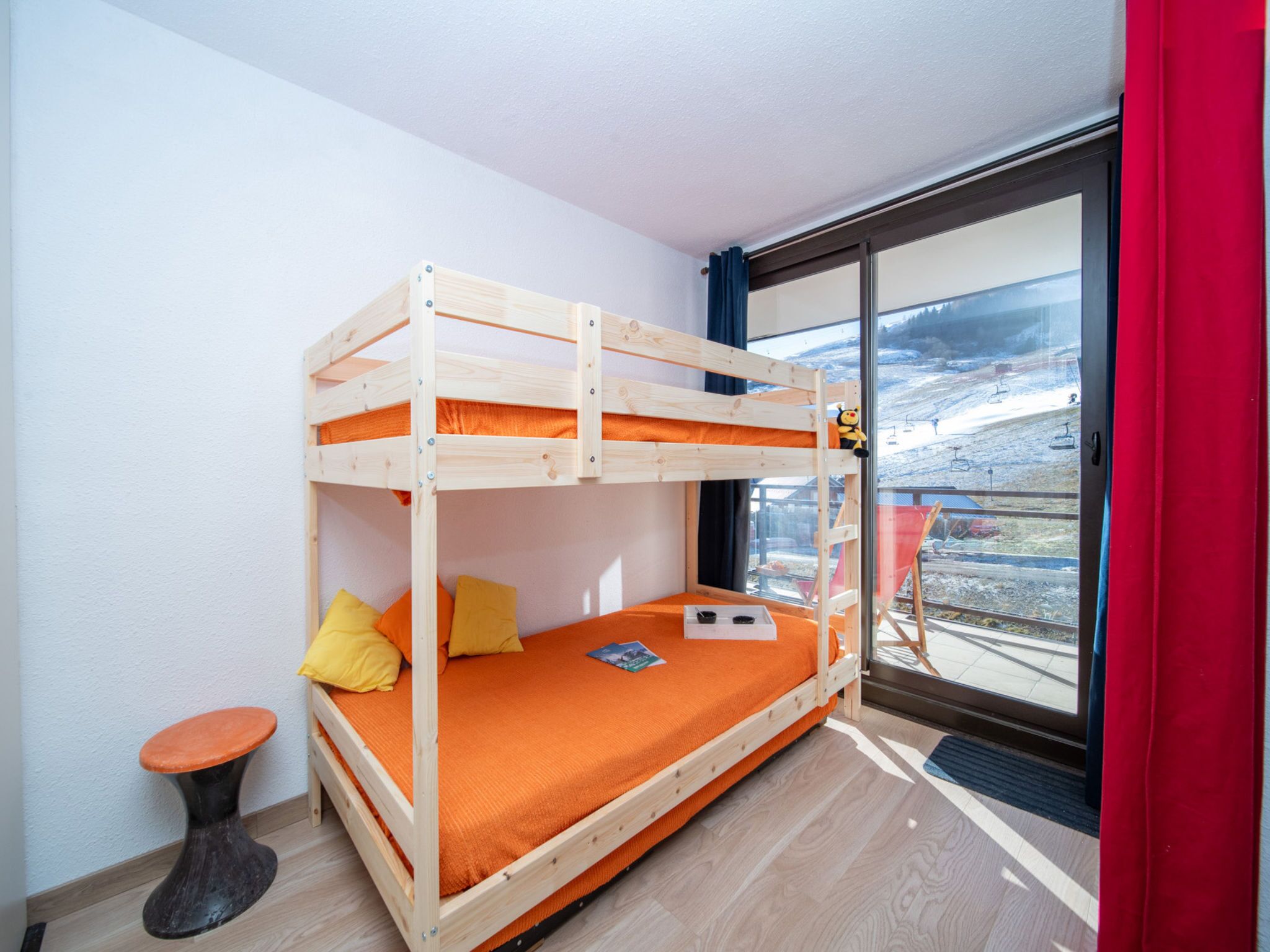 A bunk bed with orange bedding, a small stool, and a window with a view of a snowy landscape.