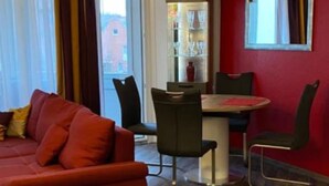 Een woonkamer met een rode bank, een eettafel met stoelen en een houten vloer.