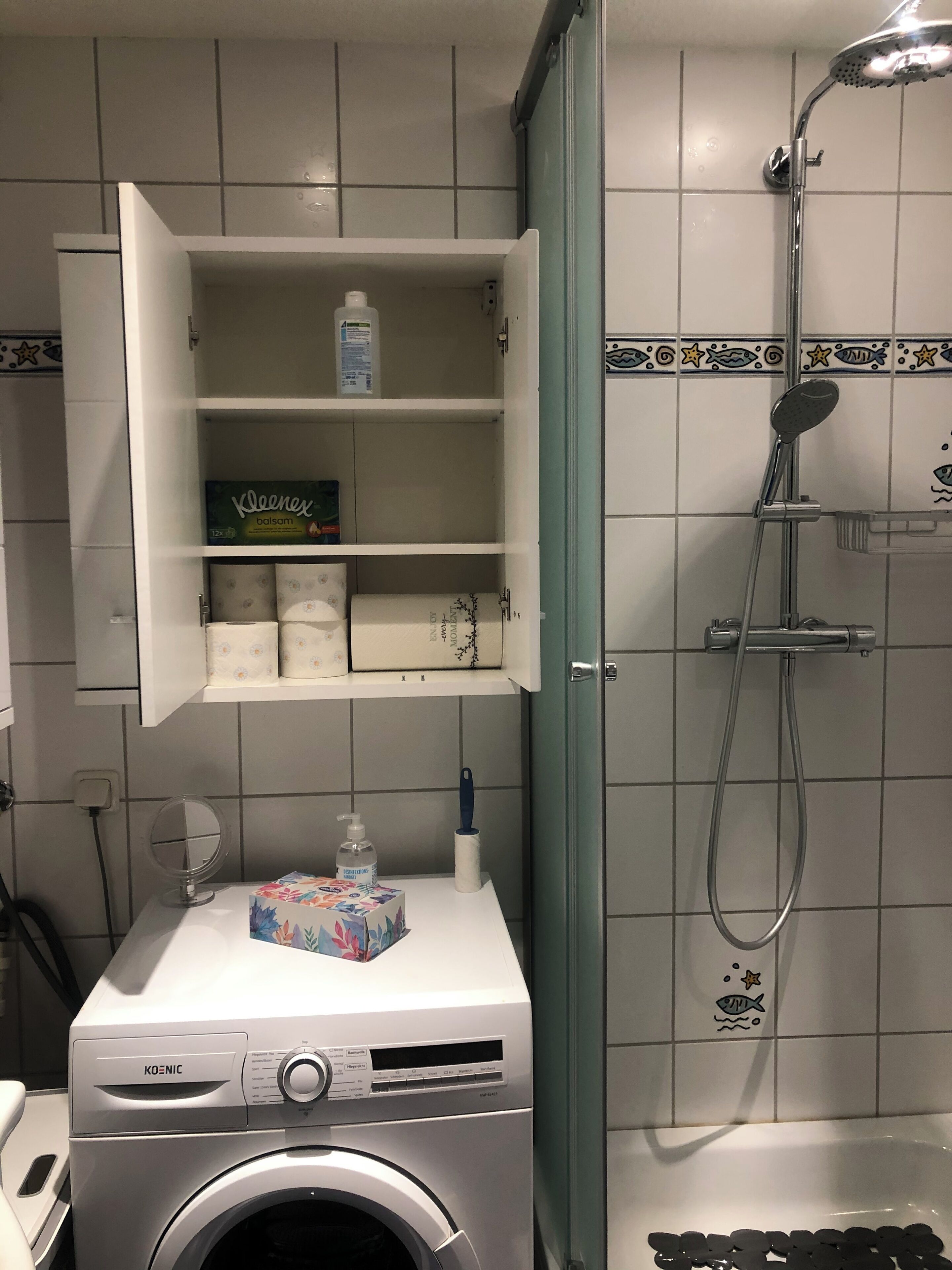Ein kleines Badezimmer mit Waschmaschine, Ablage für Pflegeprodukte und einer Duschkabine.