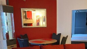 Een rode bank met een plaid, een eettafel met stoelen en een spiegel aan de muur.