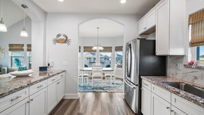 A modern kitchen with white cabinets, granite countertops, a stainless steel refrigerator, and a dining area with a view.
