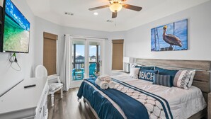 A bedroom with a bed, a ceiling fan, a TV, and a view of the outside.