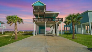 A two-story beachfront house with a balcony, a covered porch, and a garage.