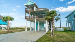 A two-story house with a balcony, a concrete driveway, and palm trees.
