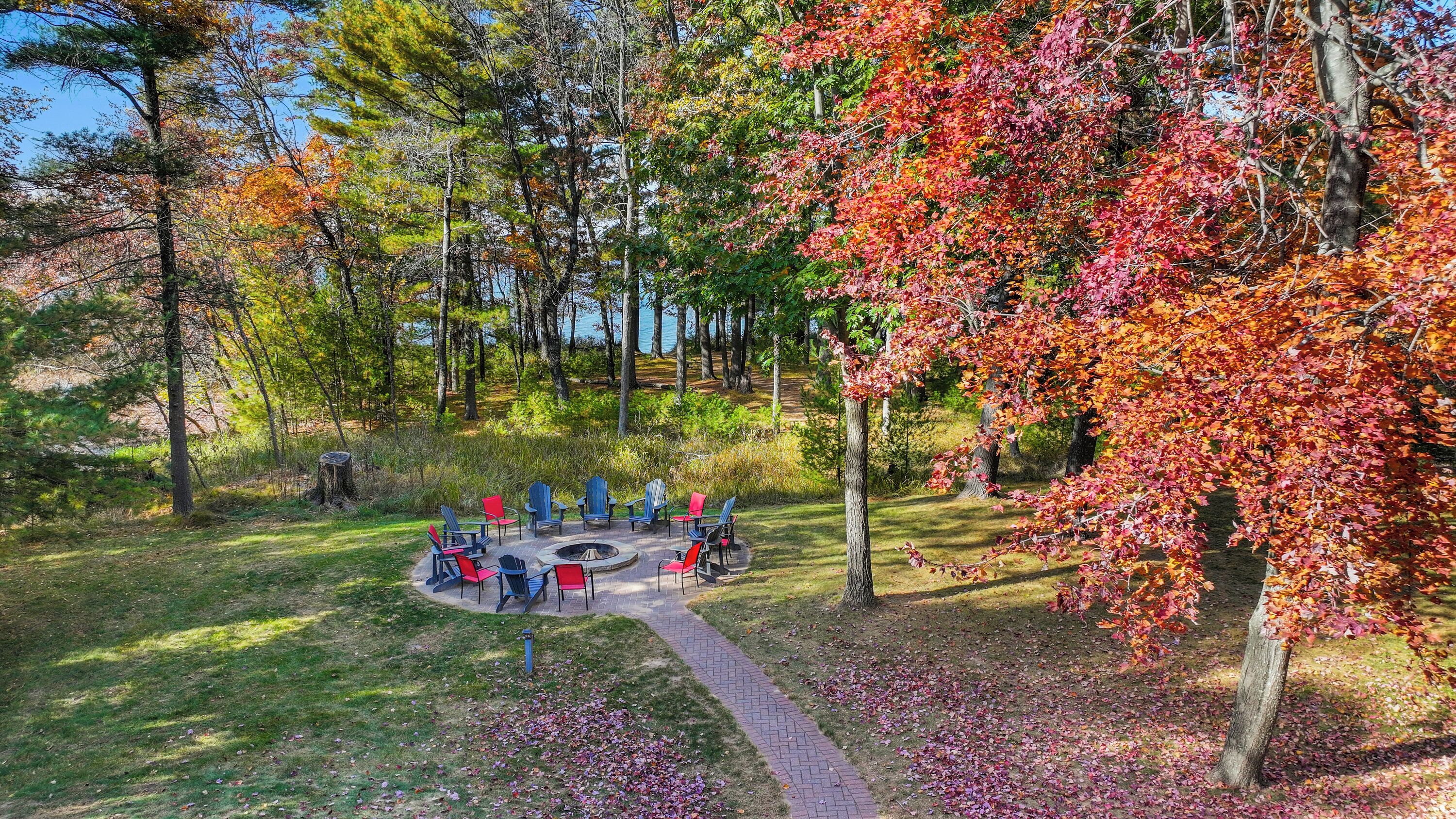 A park with a fire pit and seating area surrounded by trees with autumn foliage.