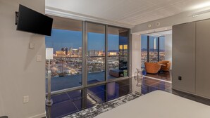 A modern hotel room with a large window offering a city view, a flat-screen TV mounted on the wall, and a comfortable seating area with a sofa and armchair. - Remodeled Strip View 1BD/1.5BA • Balcony • Sleeps 6 • No Resort Fee • Free Parking • QJ26 (Las Vegas)