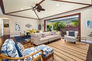 Relax in a spacious living area with a high ceiling and ceiling fan, featuring a large window with a garden view.