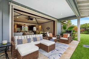 Relax in a spacious outdoor living area with a comfortable seating arrangement and dining table, surrounded by a well-maintained lawn and lush plants.
