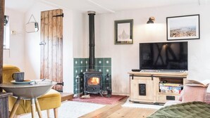 A cozy living room with a wood-burning stove, a television, and a bookshelf. - Blythburgh Cottage, Yoxford (Yoxford)