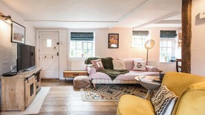 A cozy living room with a sofa, a yellow armchair, a television on a wooden cabinet, and a window with a view of the outdoors. - Blythburgh Cottage, Yoxford (Yoxford)