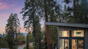 A modern cabin with large windows, surrounded by tall trees and a mountain view. - Yosemite Park / Forest View, Patio & BBQ Area (TUOLUMNE MEADOWS)
