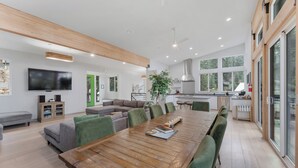 A spacious living area with a wooden dining table, green upholstered chairs, a grey sofa, a flat-screen TV, and a kitchen in the background. - Yosemite Park / Forest View, Patio & BBQ Area (TUOLUMNE MEADOWS)