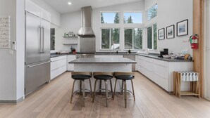 A modern kitchen with a central island, stainless steel appliances, and a large window overlooking a forested area. - Yosemite Park / Forest View, Patio & BBQ Area (TUOLUMNE MEADOWS)