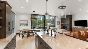 A modern kitchen with a large island, dining area, and a cozy living room with a fireplace and TV. - Whitefish Vista Retreat (Whitefish)