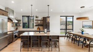 A modern kitchen with a central island, dark wooden chairs, and a dining table with chairs. - Whitefish Vista Retreat (Whitefish)