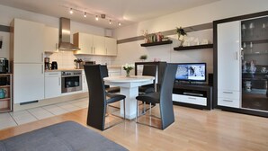 A modern kitchen with white cabinets, a dining table with black chairs, and a TV on a stand.