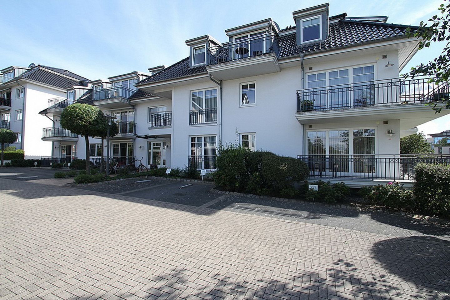 Un edificio residenziale a più piani con balconi, una strada di accesso pavimentata e un’area giardino curata.