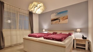A bedroom with a bed, a nightstand, a lamp, a painting on the wall, and a window with curtains.