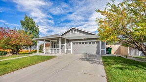 Ein eingeschossiges Haus mit einer überdachten Veranda, einer Garage und einem gepflegten Rasen.