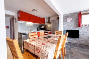 A kitchen with red cabinets, a dining table with a patterned tablecloth, and a stone fireplace.