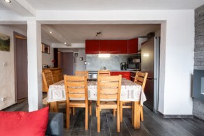A modern kitchen with red cabinets, a dining table with chairs, and a refrigerator.