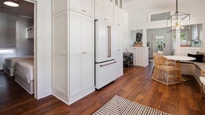 A modern kitchen with white cabinetry, a built-in refrigerator, and a dining area with wicker chairs. - Historic Cottage in Olde Town BSL - One Block from Beach & Dining (Bay St. Louis)
