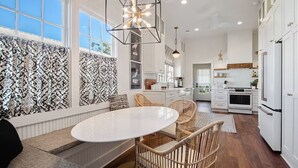 A modern kitchen with white cabinetry, a round dining table, wicker chairs, and a decorative ceiling light. - Historic Cottage in Olde Town BSL - One Block from Beach & Dining (Bay St. Louis)