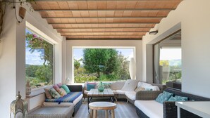 A covered outdoor seating area with wicker furniture, a wooden table, and a view of greenery. - Villa Finca Encanto with Mountain Views, Wi-Fi, and Air Conditioning (Arcos de la Frontera)