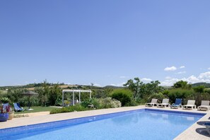A swimming pool with lounge chairs, a pergola, and a view of the countryside.