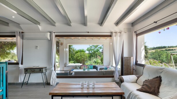 A modern interior with a sofa, a wooden table, and a view through a large window. - Villa Finca Encanto with Mountain Views, Wi-Fi, and Air Conditioning (Arcos de la Frontera)
