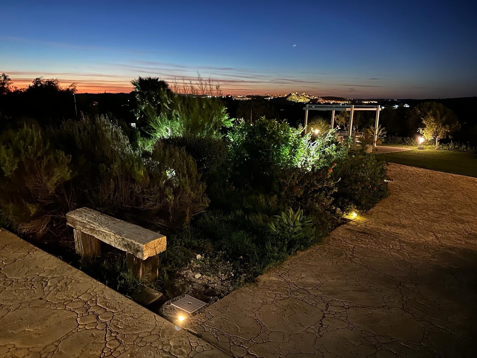 Een tuin met een stenen bank, een pergola en een pad.