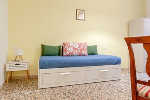 A bedroom with a bed, a nightstand, a chair, and a wall-mounted picture.