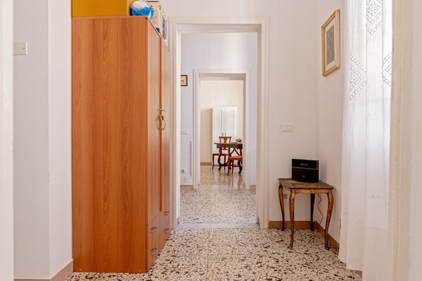 A hallway with a wooden wardrobe, a small table, and a dining area in the background.