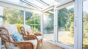 Un salón de invernadero con mobiliario de mimbre y vistas a un jardín.