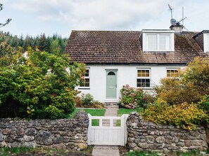 A white cottage with a green door, stone walls, and a stone gate.