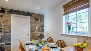 Un comedor con pared de piedra, una ventana con persianas y una mesa dispuesta con platos, tazones y un frutero.