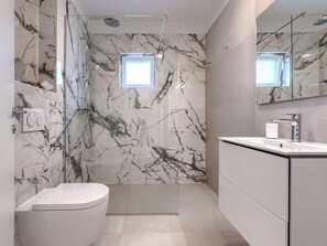 Une salle de bain moderne avec un mur en marbre, une douche en verre, des toilettes et un lavabo avec un miroir.