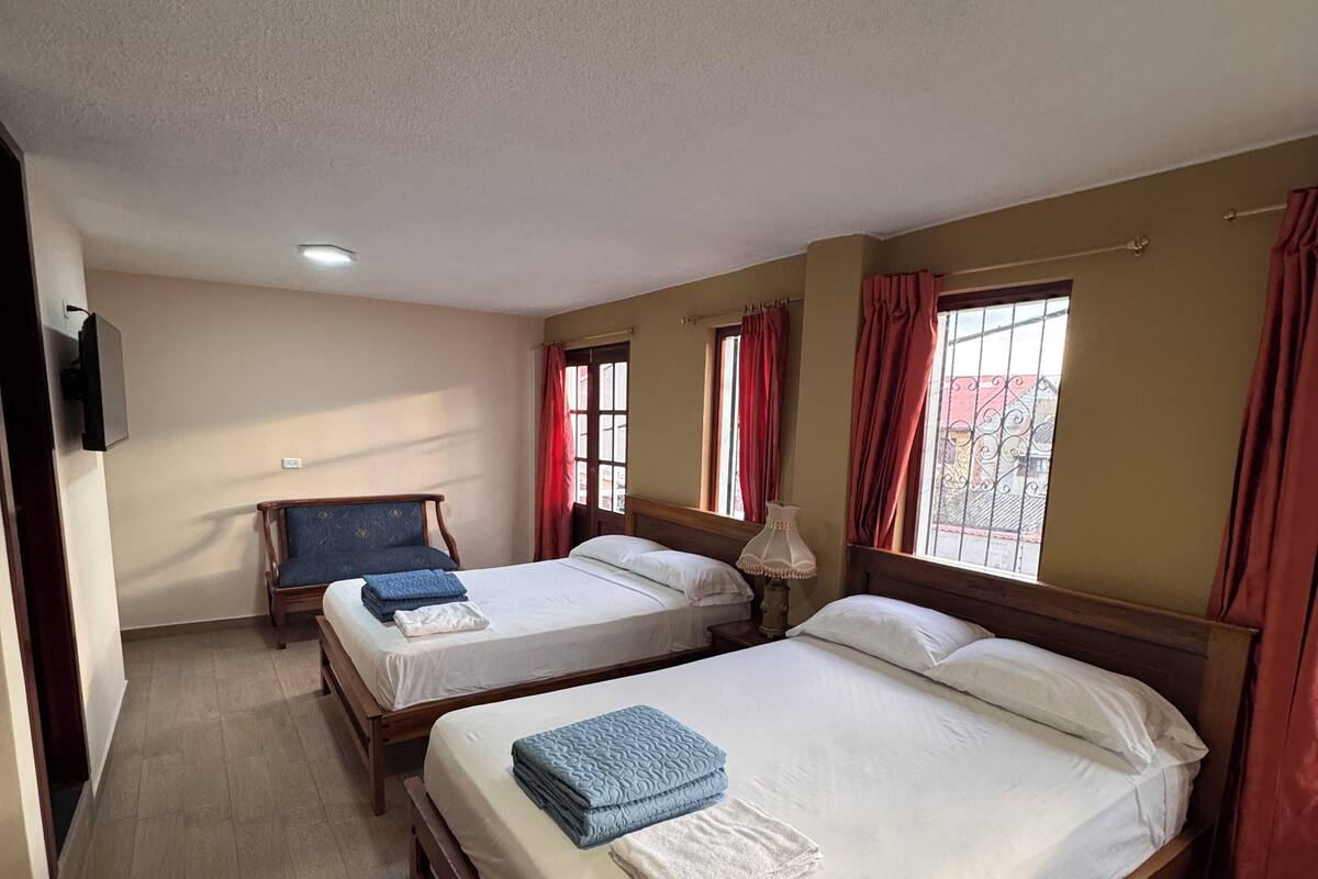 A hotel room with two wooden beds, a flat-screen TV, and a window with curtains.